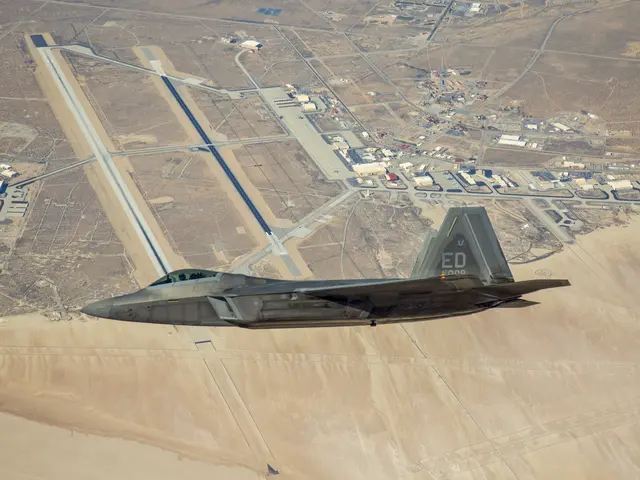 The image shows a fighter jet flying over a desert landscape, with roads and buildings visible in...