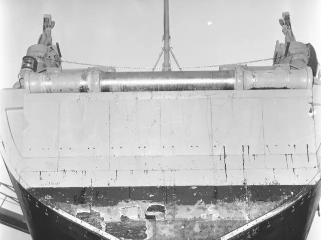 The image shows a black and white photo of a large ship in a dry dock, surrounded by poles and...