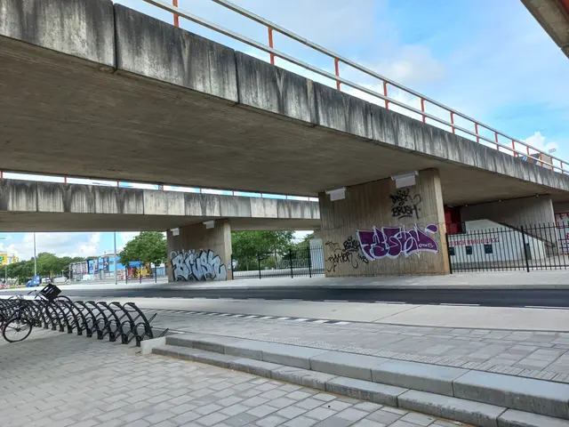 The image shows a bridge with graffiti on the side of it, a road below, a sidewalk with bicycles...