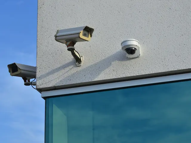The image shows two security cameras mounted on the side of a building, with a glass wall in the...