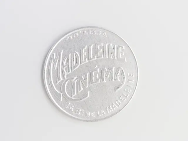 The image shows a silver coin with the words "Madeleine Cinema" written on it against a white...