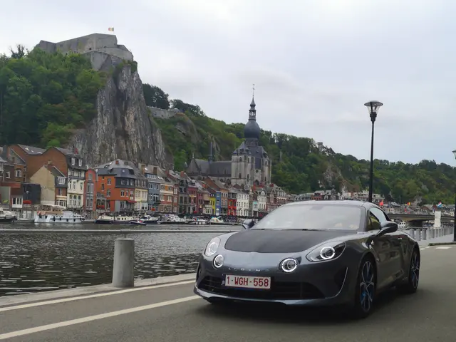 The image shows a black Porsche 911 Carrera 4S driving down a road next to a body of water, with...