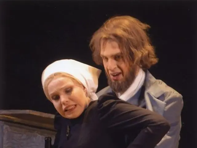 The image shows a man and woman standing next to each other on a stage, with the woman holding a...