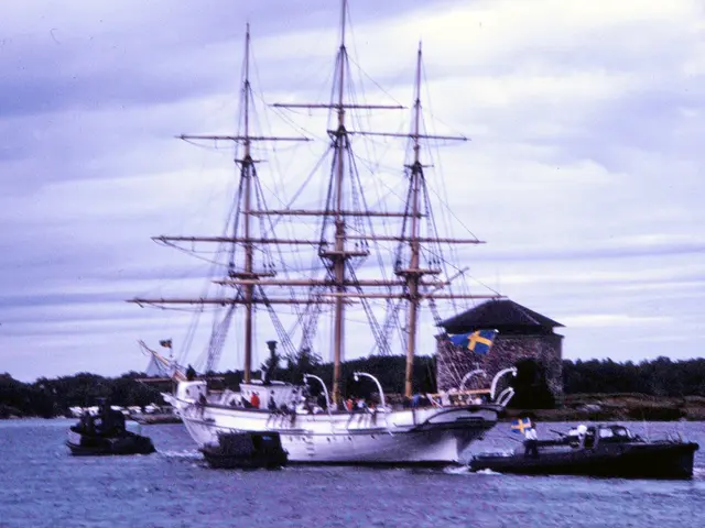 The image shows a tall ship sailing in the water near a small boat, with a few people on board. In...