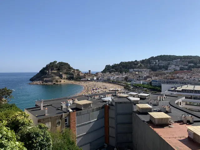 The image shows a view of a beach from the top of a building, with the ocean on the left side,...