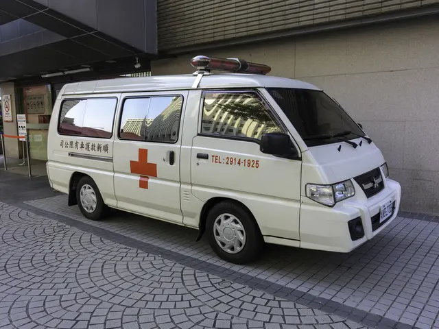 The image shows an ambulance parked in front of a building, surrounded by trees and plants. The...