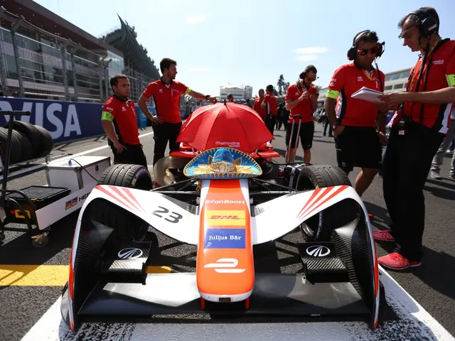 The image shows a Formula E car on the track with a group of people standing around it. The car is...