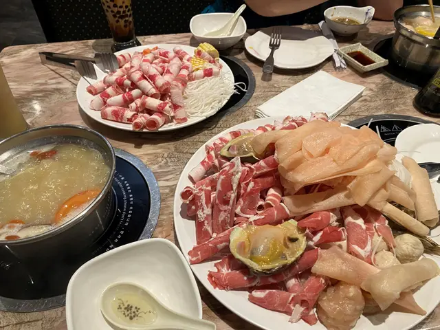 The image shows a table topped with plates of food and bowls of soup, along with spoons, forks,...