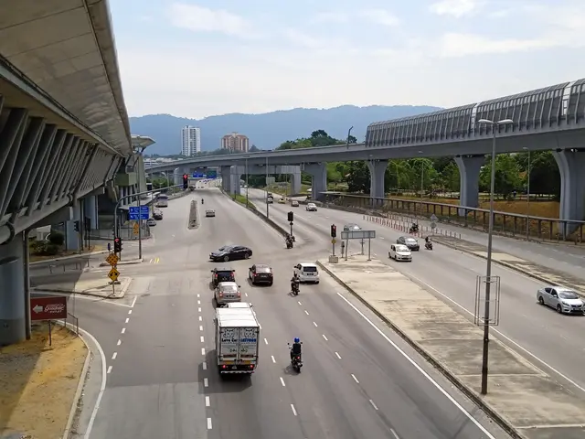 The image shows a highway filled with lots of traffic next to a bridge, with street light poles,...