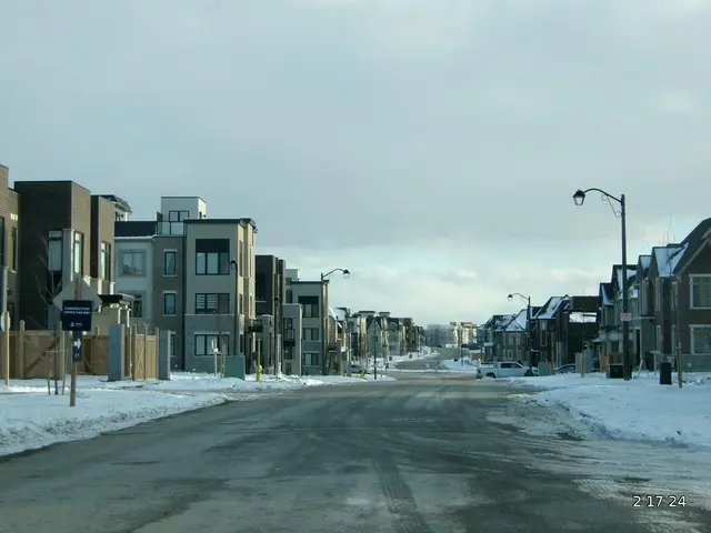 The image shows a street with snow on the ground and buildings on either side. There are vehicles...