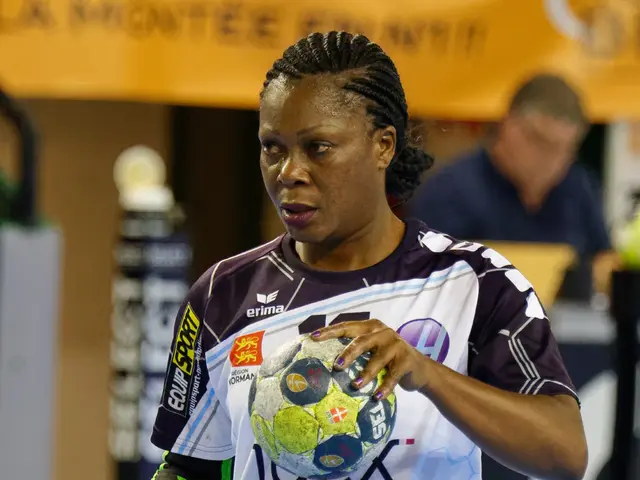 The image shows a woman in a white shirt and purple shorts holding a soccer ball, with a person...