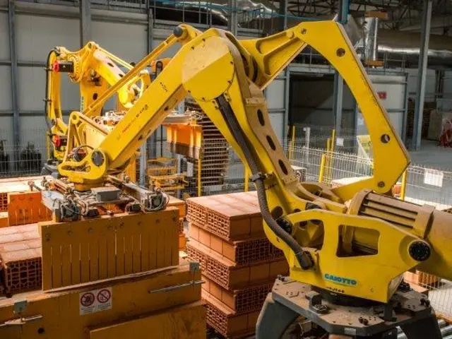 The image shows a large warehouse filled with lots of boxes and cranes, as well as a fence, poles,...