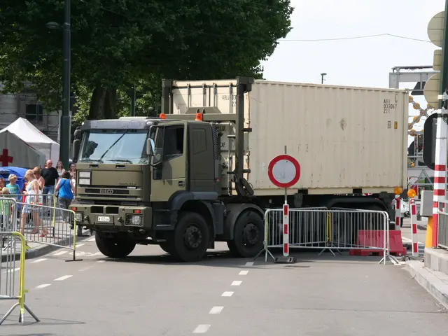 The image shows a truck parked on the side of the road, surrounded by a group of people standing on...