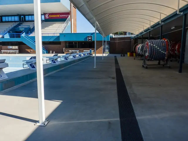 The image shows a large indoor swimming pool with a lot of chairs and a building in the background....