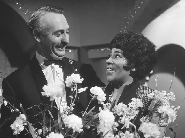 The image shows a man and woman in tuxedos standing next to each other, both of them smiling and...