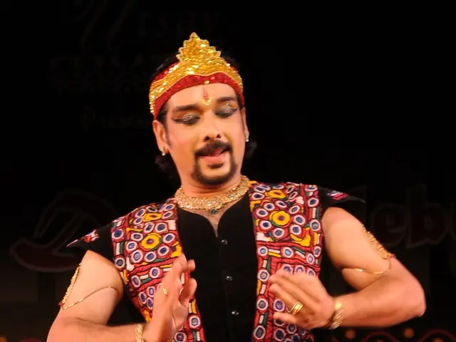 The image shows a man in a red and black outfit performing a dance on a stage, with a dark...