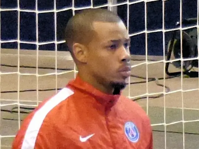 The image shows a man standing in front of a goal, holding a soccer ball in his hands. He is...