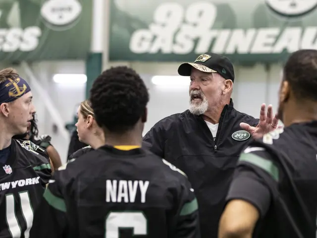 The image shows a group of men standing around each other on a field, with a man wearing a cap in...