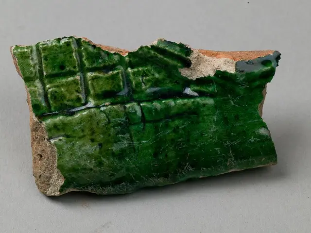 The image shows a piece of green glazed pottery on a grey surface. The pottery has a glossy finish...