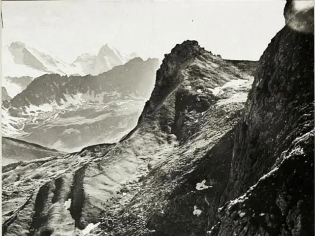 The image shows a black and white photo of a mountain range with snow-capped peaks in the...