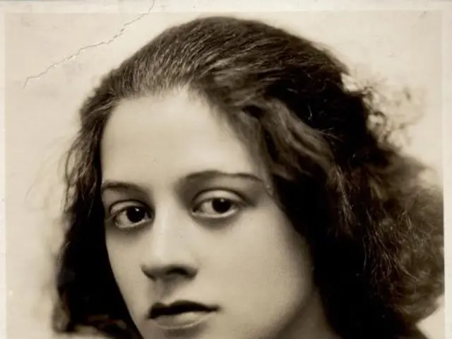 The image shows a black and white photo of a woman with curly hair. She is looking directly at the...