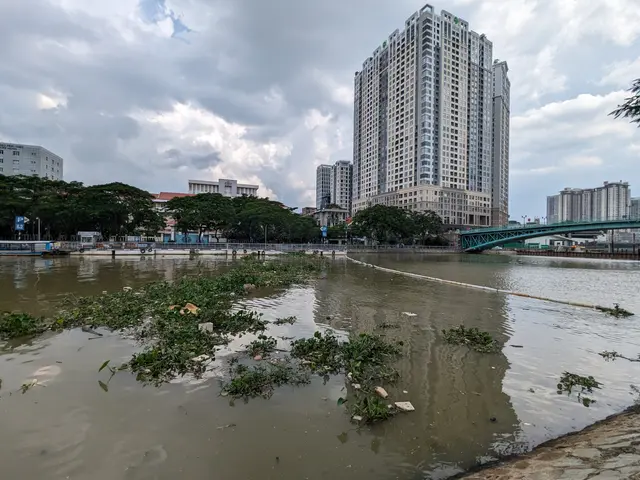 The image shows a flooded street with tall buildings in the background, a bridge on the right side,...