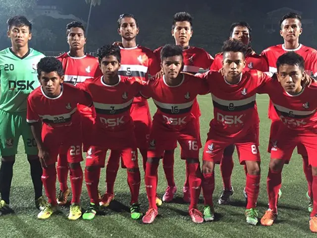 The image shows a group of men standing on top of a soccer field, illuminated by the lights of the...