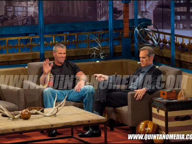 It is a media interview there are two people sitting on the sofa adjacent to each other in front of...