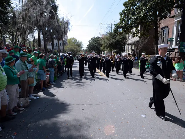 The image shows a group of people walking down a street in a St. Patrick's Day parade. The people...
