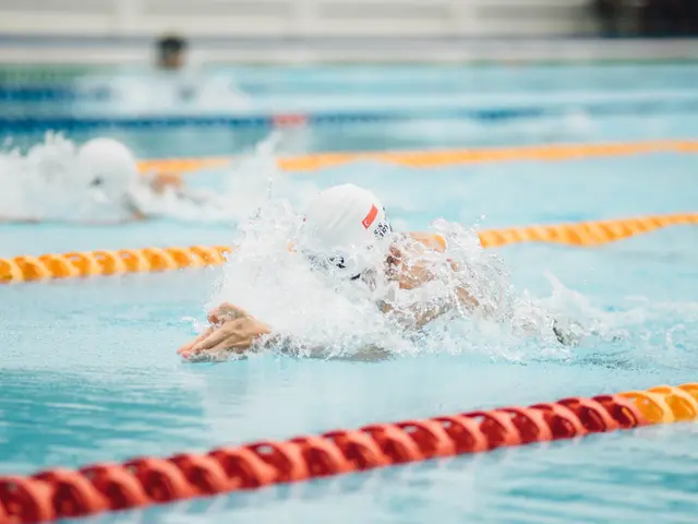 The image shows two swimmers in a swimming pool with their arms outstretched, competing in a...