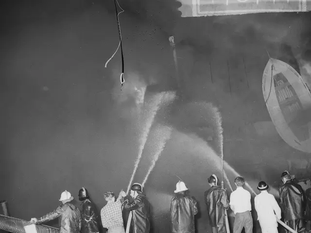 The image shows a group of firefighters wearing helmets and holding pipes, spraying water on a...