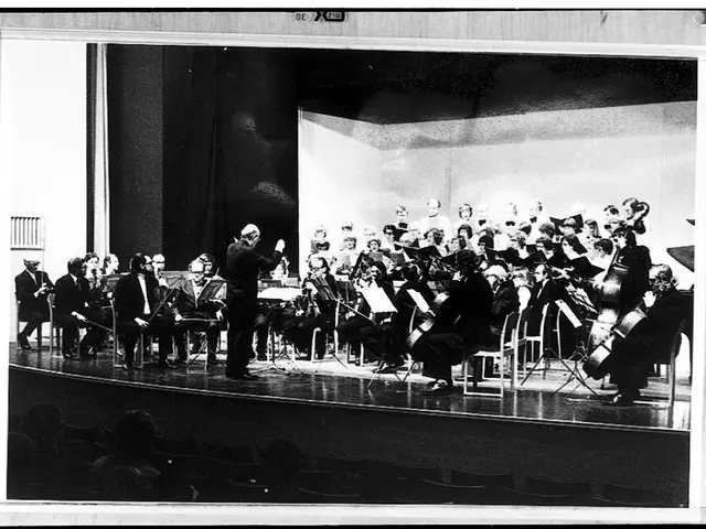 The image shows a black and white photo of a conductor standing on a stage in front of an orchestra...