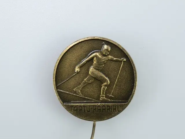 The image shows a gold medal with a skier on it, depicting a person holding two sticks in their...