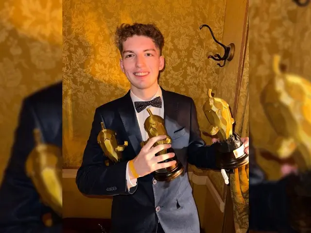 The image shows a man in a tuxedo holding an Oscar statue, with a wall in the background and a...
