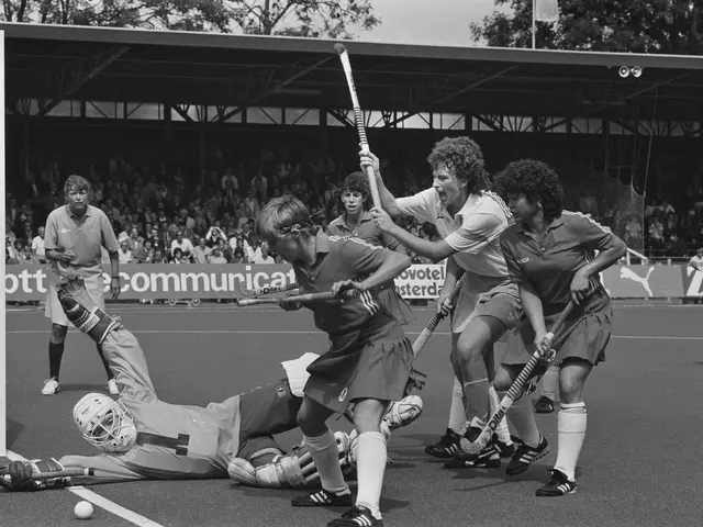 The image shows a group of women playing a game of field hockey. They are wearing helmets and...