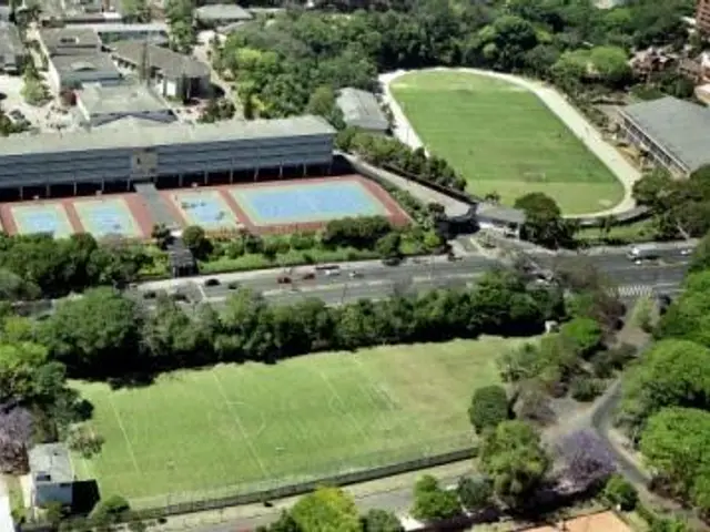 The image shows an aerial view of a soccer field in the middle of a city, surrounded by trees,...