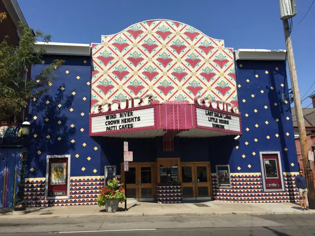 The image shows a blue building with a colorful mural on the side of it, surrounded by trees, light...