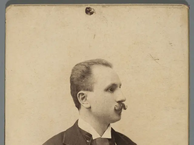 The image shows an old photo of a man in a tuxedo with a mustache. He has a serious expression on...