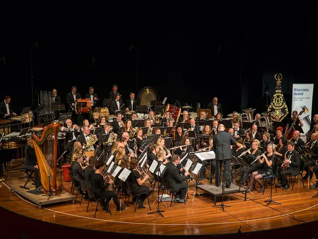 The image shows a large group of people on a stage playing musical instruments, with mics and...