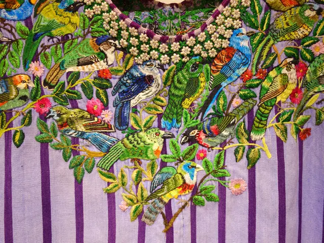 The image shows a close up of a dress with intricate embroidery of birds and flowers on it. The...