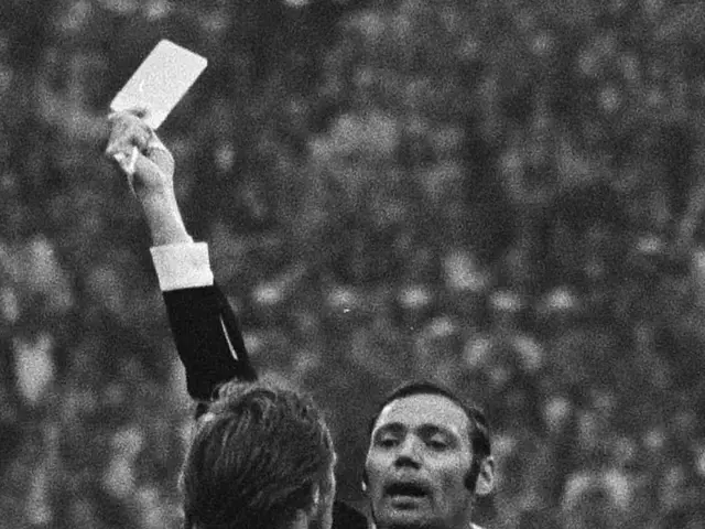 The image shows a referee holding up a white card to a soccer player in a black and white photo....