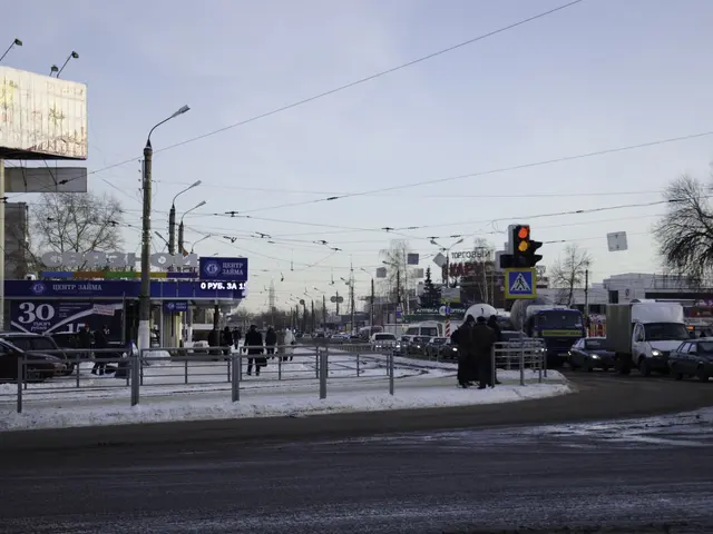 The image shows a city street filled with lots of traffic on a snowy day. There are street lights,...
