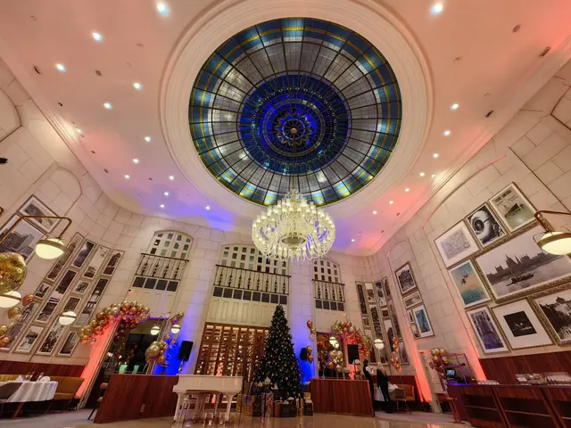 The image shows a large room with a chandelier hanging from the ceiling, a Christmas tree in the...