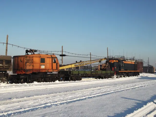 The image shows a freight train traveling down train tracks covered in snow, with electric poles...