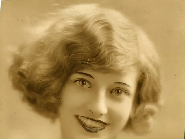 The image shows an old photo of a woman with a warm smile on her face. She is wearing a dress and...