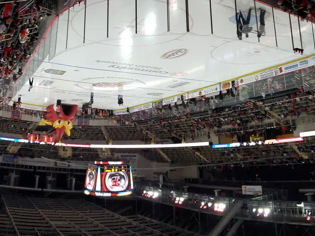 The image shows a large arena filled with lots of people watching a hockey game. There are chairs,...