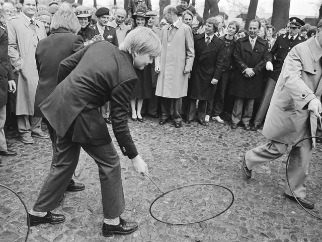 The image shows a man and woman playing with a hula hoop in front of a crowd of people, some of...