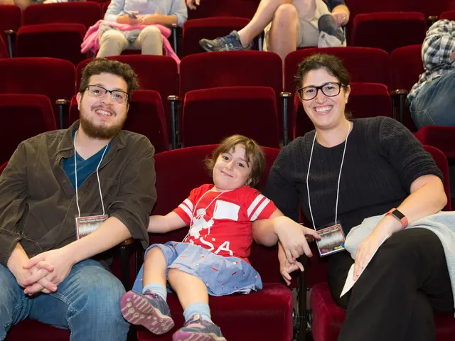 The image shows a family of three - a man, woman and a child - sitting in a movie theater. The man...