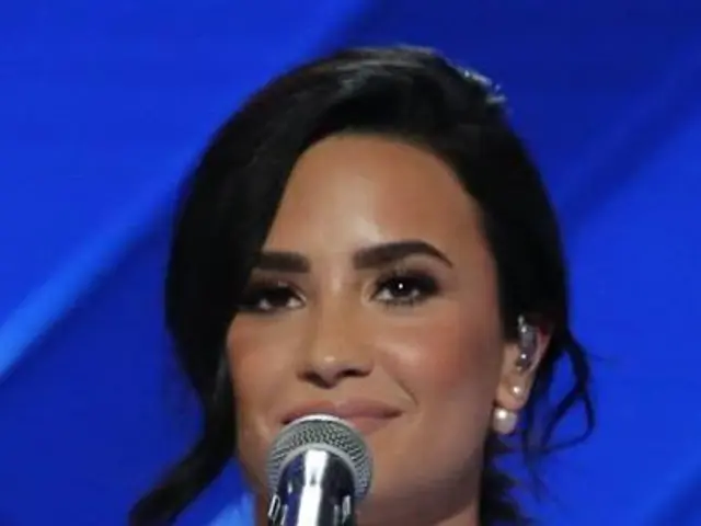 The image shows Demi Lovato standing in front of a microphone at the Grammys, with a blue...