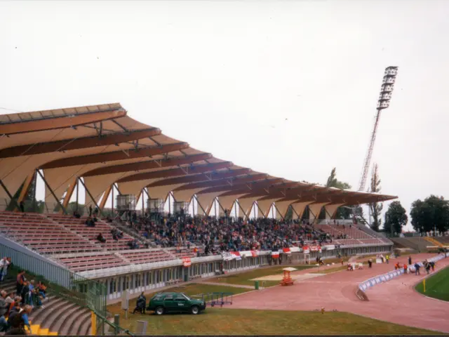 The image shows an old photo of a stadium with a lot of people in it. We can see a group of people...